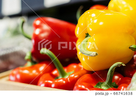 Side view of yellow bell pepper lying on red peppers on the shelf. Close-up of fresh agricultural vegetables in grocery. Vegeterian food, dieting, healthy eating. Side view of yellow bell pepper lying on red peppers on the shelf. Close-up of fresh agricultural vegetables in grocery. Vegeterian food, dieting, healthy eating. 66741638