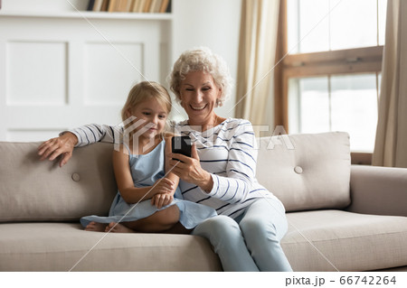 Old granny little granddaughter sitting on couch with smartphone 66742264