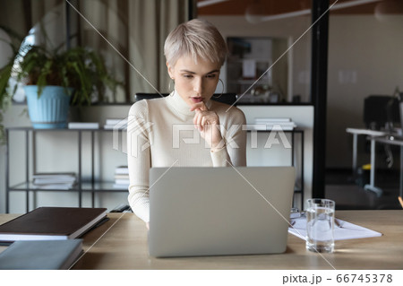 Concentrated businesswoman working using laptop sitting at desk in office 66745378