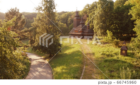 Brown wooden church with three domes in the forest and asphalt road. 66745960