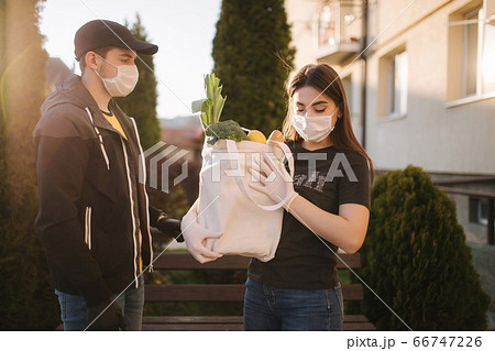 Courier in protective mask and medical gloves delivers fresh food for female customer. Delivery service under quarantine. Coronavirus covid-19 theme 66747226