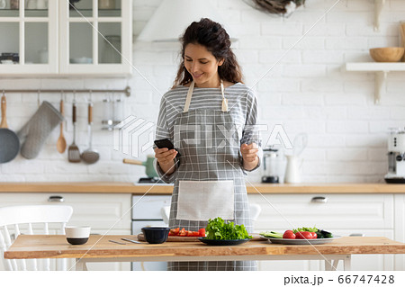 Happy young attractive woman cooking to recipe on smartphone. 66747428