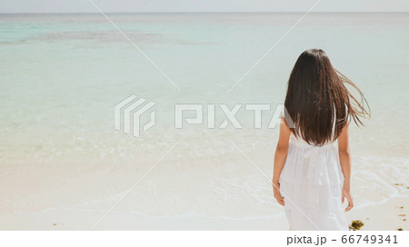 A charming philippine schoolgirl in a white dress is walking along a white sandy beach. Enjoying the tropical scenery. Childhood. 66749341