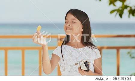 Philippine schoolgirl in white dress smiles, eating crispy potato chips. Tropical landscape. The palms. Summer. 66749352