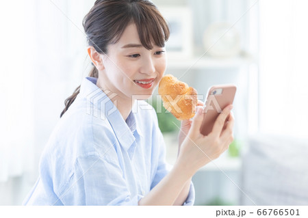 クロワッサンを食べながらスマホを見る若い女性 66766501