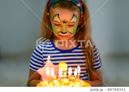 A child in makeup looks at a birthday cake 66769341