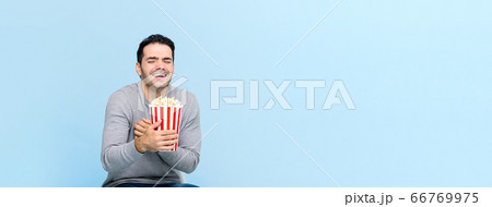 Young man holding popcorn laughing while watching movie Young man holding popcorn laughing while watching movie 66769975