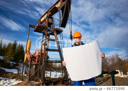 Oil worker standing in the oilfield next to a pump jack with a big paper Oil worker standing in the oilfield next to a pump jack with a big paper 66772090