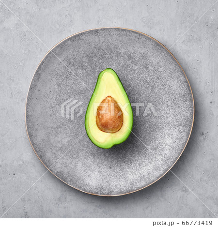 Half Avocado in gray hand made matte plate on concrete rough backdrop. Grey ceramic saucer setting. Half Avocado in gray hand made matte plate on concrete rough backdrop. Grey ceramic saucer setting. 66773419