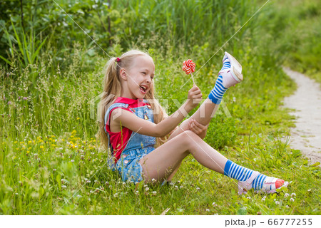 Blonde little girl with long hair and candy on a stick 66777255