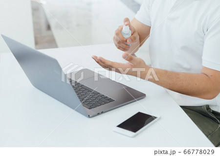 A man using the spray while working at home with his mask on A man using the spray while working at home with his mask on 66778029