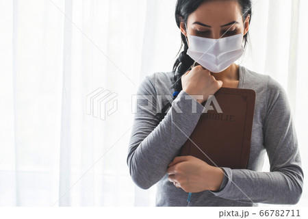 Portrait of a woman with a surgical mask on her while praying with the Bible in hand 66782711