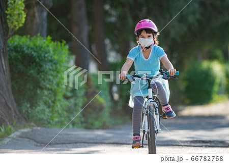 Little girl in protective medical mask rides a bike Little girl in protective medical mask rides a bike 66782768