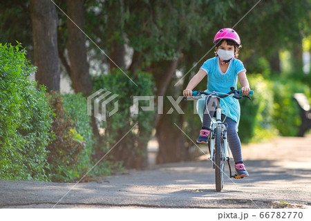 Little girl in protective medical mask rides a bike Little girl in protective medical mask rides a bike 66782770