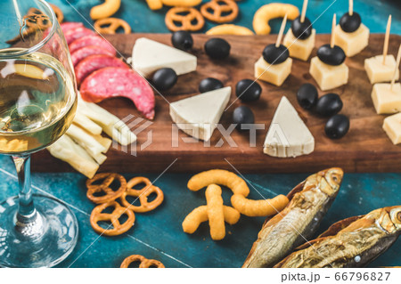 Pepperoni slices, cheese and black olives on a wooden board with crackers and a glass of white wine Pepperoni slices, cheese and black olives on a wooden board with crackers and a glass of white wine 66796827