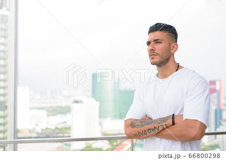 Young handsome bearded Persian man looking at view of the city Young handsome bearded Persian man looking at view of the city 66800298