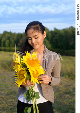 Young beautiful Asian woman holding bouquet of sunflowers against relaxing view of nature Young beautiful Asian woman holding bouquet of sunflowers against relaxing view of nature 66800339