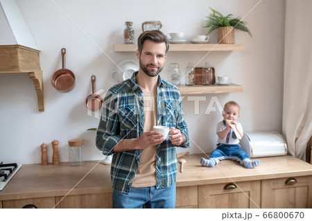 Young father standing with a cup in his hands, his little son sitting on the table 66800670