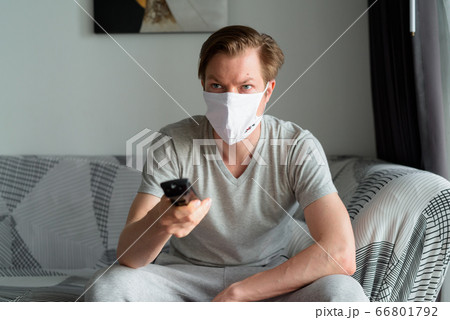 Young man with mask watching tv and staying at home under quarantine Young man with mask watching tv and staying at home under quarantine 66801792