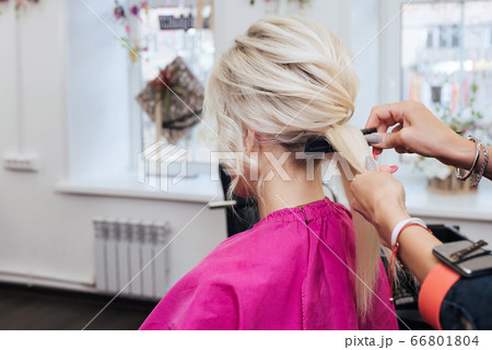 hands of a professional hairstylist make a hairstyle for a blonde girl with long hair 66801804