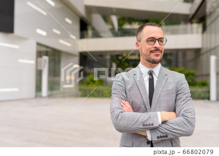 Handsome Hispanic bald bearded businessman thinking with arms crossed in the city Handsome Hispanic bald bearded businessman thinking with arms crossed in the city 66802079