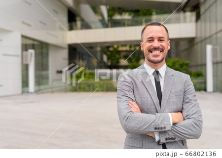 Happy Hispanic bald bearded businessman smiling with arms crossed in the city outdoors Happy Hispanic bald bearded businessman smiling with arms crossed in the city outdoors 66802136