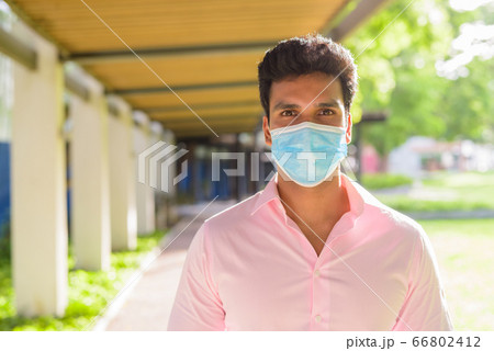 Face of young Indian businessman with mask for protection from corona virus outbreak at the park Face of young Indian businessman with mask for protection from corona virus outbreak at the park 66802412