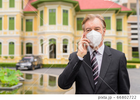 Mature businessman with mask talking on the phone in the city outdoors 66802722