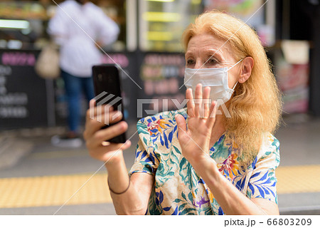 Blonde senior woman with mask video calling at the coffee shop outdoors 66803209