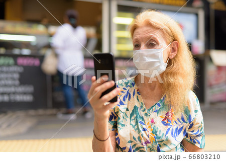 Blonde senior woman with mask using phone at the coffee shop outdoors 66803210