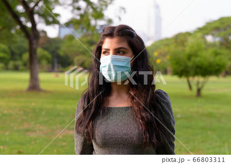 Young Indian woman with mask thinking while relaxing at the park Young Indian woman with mask thinking while relaxing at the park 66803311