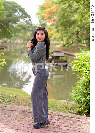 Full body shot of happy young beautiful Indian woman looking back at the park outdoors 66803418