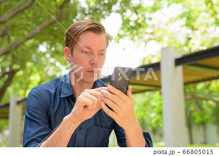 Face of young handsome blond businessman using phone at the park outdoors Face of young handsome blond businessman using phone at the park outdoors 66805015