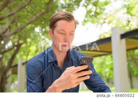 Face of young handsome blond businessman using phone at the park outdoors Face of young handsome blond businessman using phone at the park outdoors 66805022