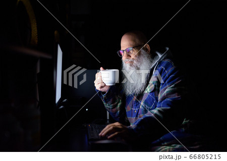 Happy mature bald bearded hipster man drinking coffee while working overtime at home late at night 66805215