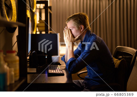 Stressed young businessman looking tired while working overtime at home late at night Stressed young businessman looking tired while working overtime at home late at night 66805369