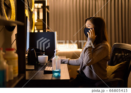 Young Asian woman with mask talking on the phone while working from home at night 66805415