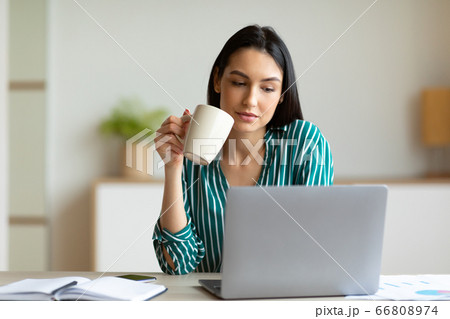 Office Girl At Laptop Having Coffee Sitting At Workplace Indoors 66808974