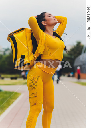 Young woman in yellow shirt delivering food using gadgets to track order at the city's street. Courier using online app for receiving payment and tracking shipping address. Modern technologies. Young woman in yellow shirt delivering food using gadgets to track order at the city's street. Courier using online app for receiving payment and tracking shipping address. Modern technologies. 66810444
