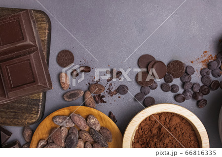 Chocolate pieces and drops, cocoa beans and powder on grey background Chocolate pieces and drops, cocoa beans and powder on grey background 66816335
