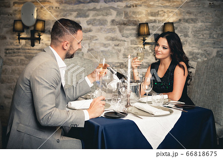 Romance and dating concept. Young couple man and woman with champagne glasses celebrating and toasting in restaurant. Two people male and female in elegant evening suit and dress on romantic dinner 66818675