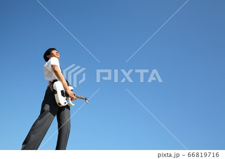 青空を背景に屋外でエレキギターを演奏する男子高校生 66819716