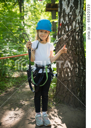 Rope adventure - a little girl with an insurance belt standing in the forest and holding an insurance hook 66820339