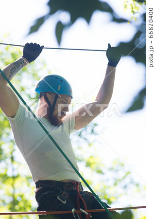 Rope adventure - man about to walk on the suspension rope bridge and holding by the rope above his head 66820400