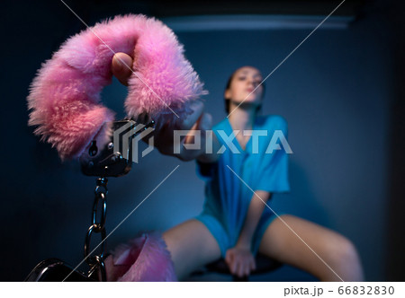 Young woman giving fluffy pink handcuffs on blue background Young woman giving fluffy pink handcuffs on blue background 66832830