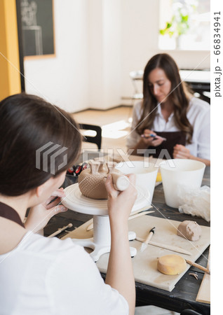 Closeup of bottom of mug, which is being decorated in ceramic studio. Female professional hands making clay dots or drops on the surface of vase by special squeezing tool. 66834941