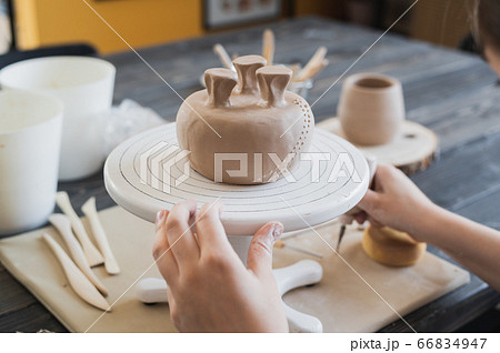 Closeup of bottom of mug, which is being decorated in ceramic studio. Female professional hands making clay dots or drops on the surface of vase by special squeezing tool. 66834947