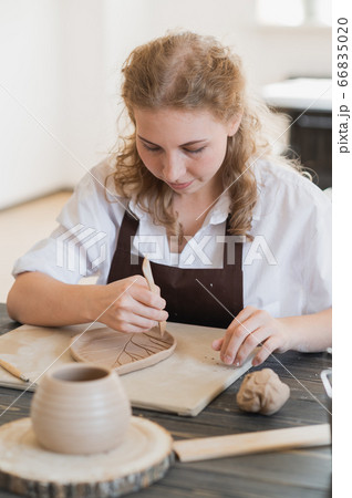 Female hands holding stick and making ornament on decorative product. Clay master moulding clay on a pottery and ceramics workshop. Female hands holding stick and making ornament on decorative product. Clay master moulding clay on a pottery and ceramics workshop. 66835020
