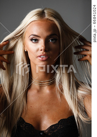 Portrait of blond young woman with beautiful makeup and hairstyle in a black lace dress stands on gray background. Fashion model poses in elegant clothes in studio 66841024