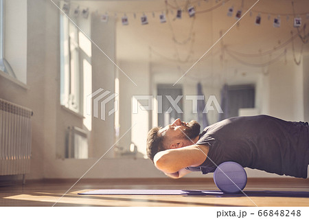Bearded man lying on foam roller during training in studio 66848248